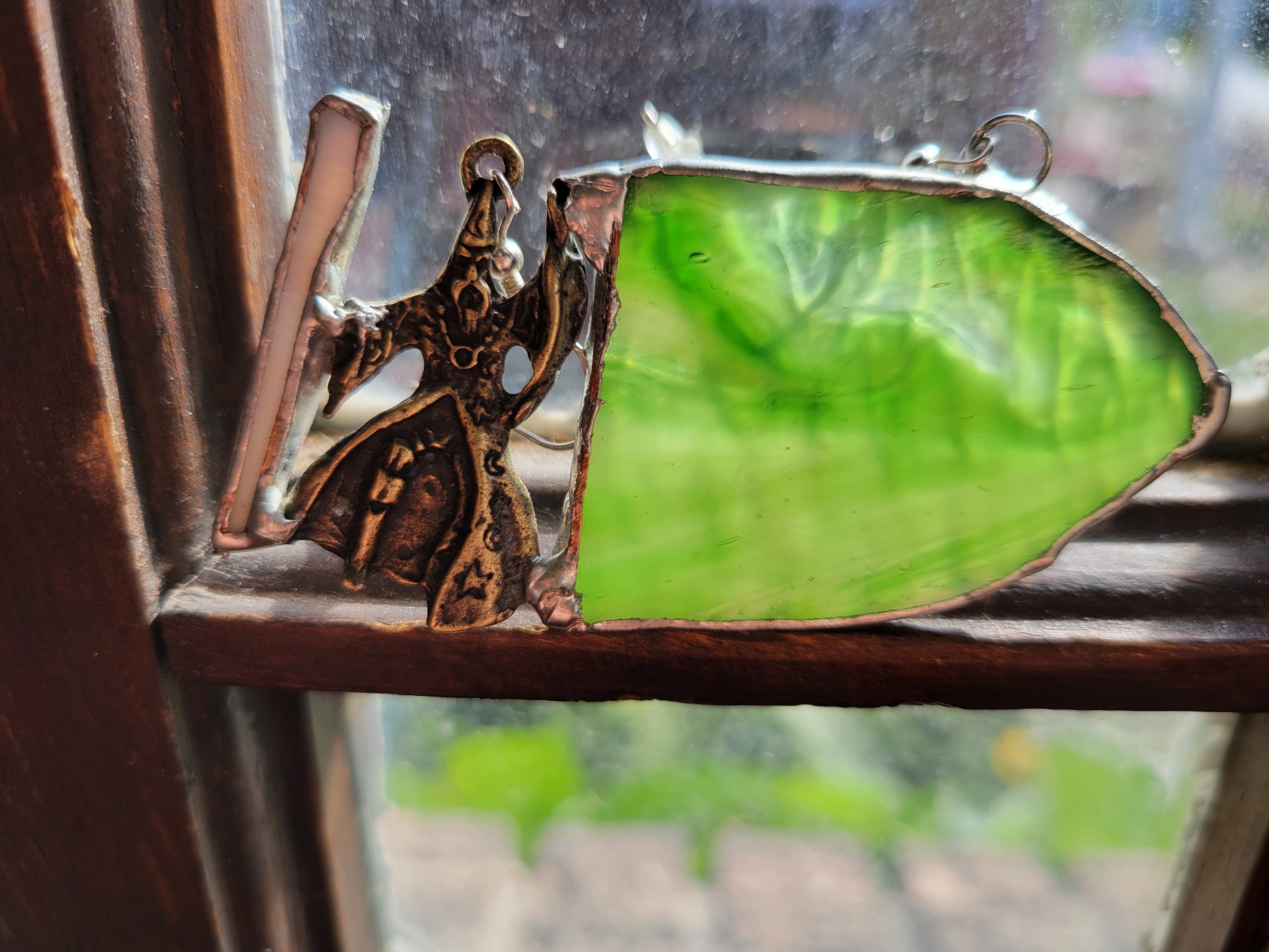 Custom earring with a small brass wizard next to a piece of green glass.